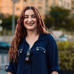 A cheerful woman with wavy hair smiles in an urban park. Captured outdoors.