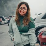 A smiling woman stands outdoors in foggy Tagaytay, Philippines, surrounded by parked cars.