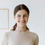 A young woman smiling indoors in a minimalist room, emitting a warm and inviting vibe.